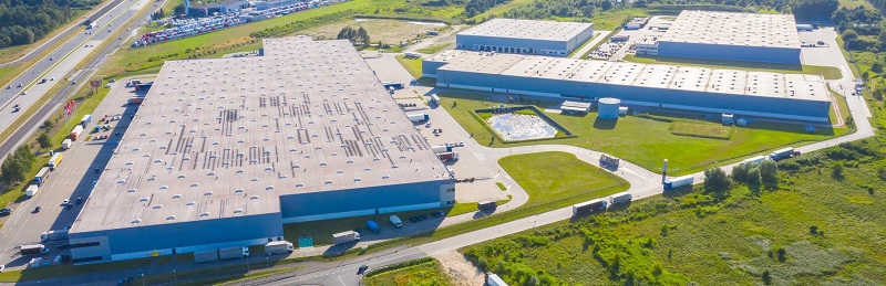 Aerial Top View of Industrial Storage Building Area with Solar Panels on the Roof and Many Trucks Unloading Merchandise.